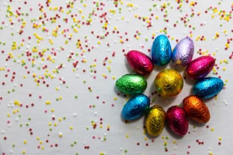 Many aligned colored chocolate easter eggs on white background and colorful c Stock Photos
