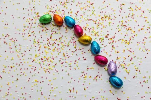 Many aligned colored chocolate easter eggs on white background and colorful c Stock Photos