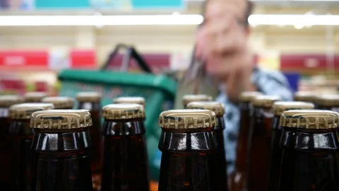 Many beer bottles on a retail display and a man with a shopping cart takes a few Stock Footage 281583548