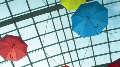 Many bright colored umbrellas suspend under a transparent glass ceiling in Stock Footage 119990644