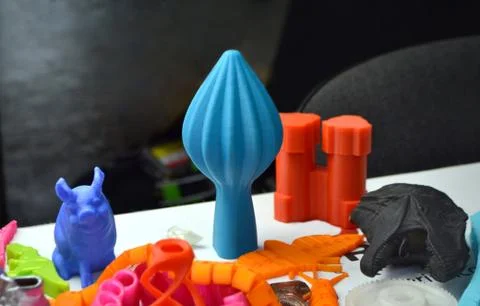 Many bright multi-colored objects printed on 3d printer lie on flat surface Foto stock