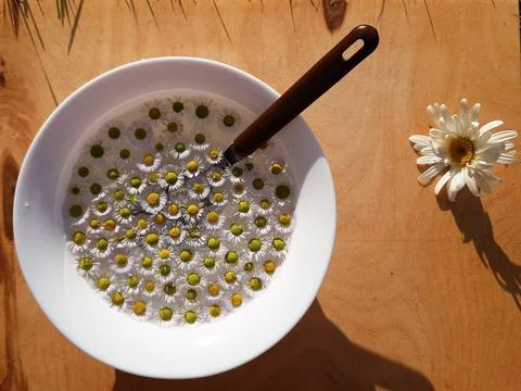 Many chamomile inflorescences lie in a plate on a wooden background. the spoo Stock Photos