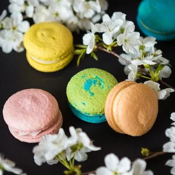 Many colored macaroons on a black background with white apple blossom Stock Photos