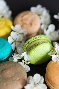 Many colored macaroons on a black background with white apple blossom Stock Photos