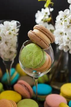 Many colored macaroons on a black background with white apple blossom Stock Photos
