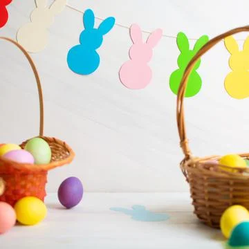 Many colorful Easter eggs in wicker basket with paper bunnies garland Stock Photos