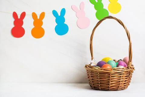 Many colorful Easter eggs in wicker basket with paper bunnies garland Stock Photos