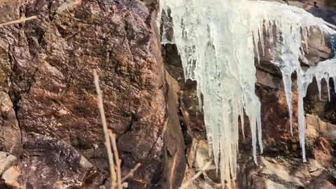 Many crowded massive icicles melting in the spring sun on a mountainside Video stock 331041755