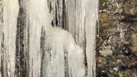 Many crowded massive icicles melting in the spring sun on a mountainside Video stock 331042182