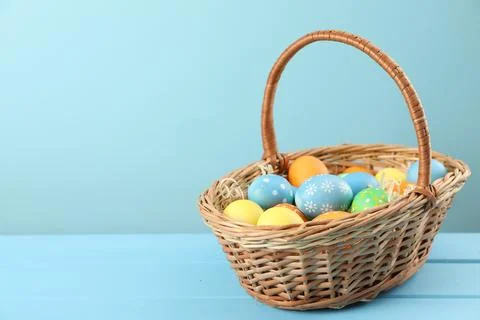 Many decorated Easter eggs in wicker basket on light blue wooden table, spa.. Stock Photos