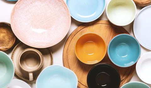 Many different ceramic plates and bowls on a light background, top view. Stock Photos