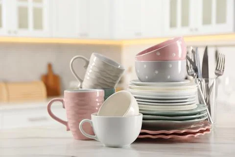 Many different clean dishware and cups on white marble table in kitchen. Sp.. Stock Photos