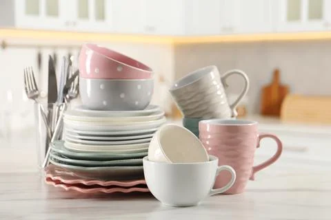Many different clean dishware and cups on white marble table in kitchen Stock Photos