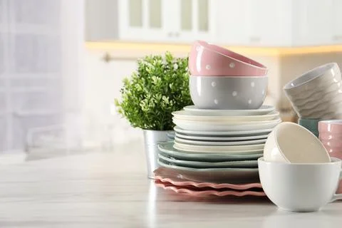 Many different clean dishware, cups and houseplant on white marble table in.. Stock Photos