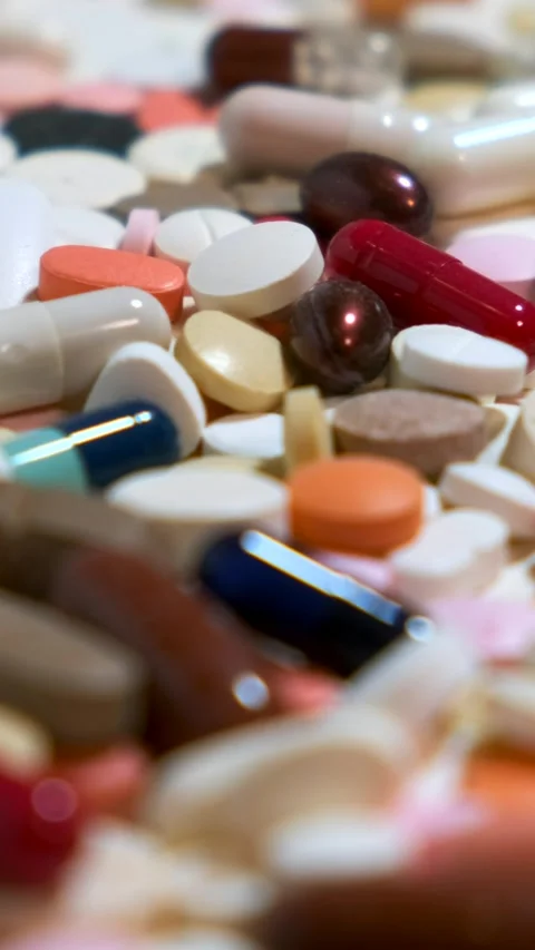 Many different colored pills are scattered on the white wooden table. Movem.. Vídeo Stock 291951744