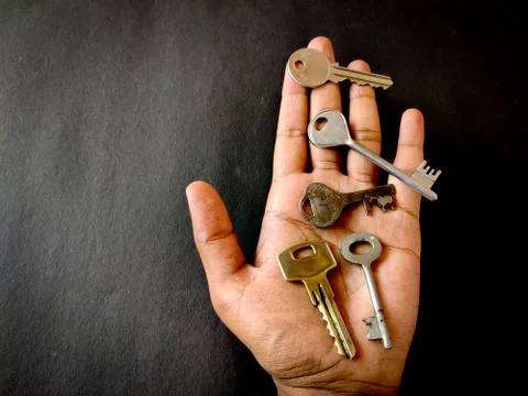 Many different sized door keys are in hands of man. Black background. Insuran Stock Photos