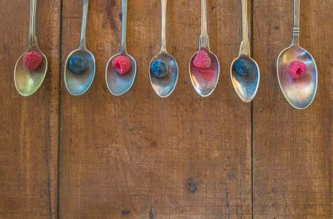 Many different vintage spoons with raspberry and blackberries on wooden backg Stock Photos