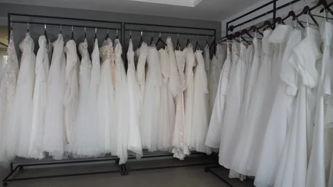 Many different wedding dresses are hanging on hangers in a modern wedding salon. Stock Footage 297845699