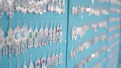 Many earrings hang on a blue wall in a shop for sale, showcasing beautiful .. Stock Footage 332475344