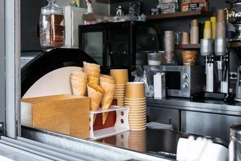 Many empty baked waffle cones and paper cups for ice cream stacked at display Stock Photos
