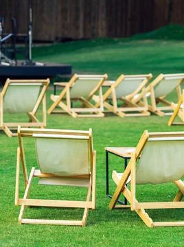 Many empty white deck chairs with tables in lawn is surrounded by shady green Stock Photos