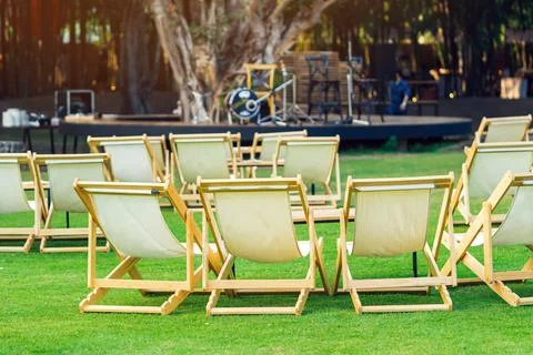 Many empty white deck chairs with tables in lawn is surrounded by shady green Stock Photos