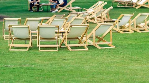 Many empty white deck chairs with tables in lawn is surrounded by shady green Stock Photos