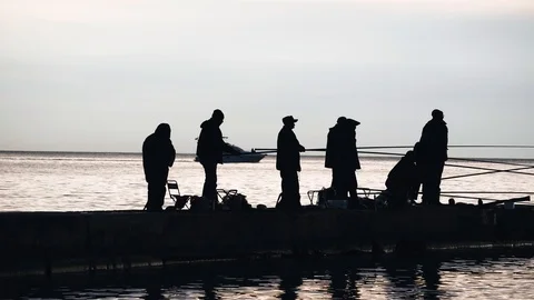 Many fishermen stand on the pier and catch fish. Cool sunset. A boat sails by. Stock Footage 123111653