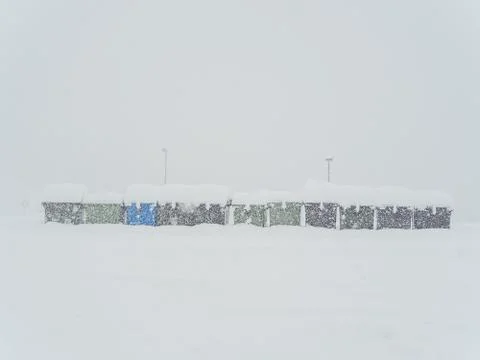 Many garbage cans stand in a row strewn with snow on the street during heavy Stock Photos