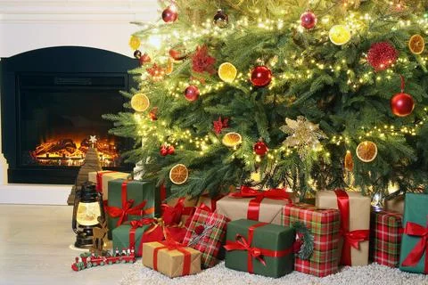 Many gift boxes, decorative elements and Christmas tree near fireplace at hom Stock Photos