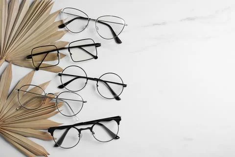 Many glasses in stylish frames and leaves on white marble table, flat lay. .. Foto stock