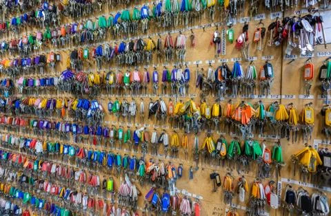 Many keys with colorful plastic key tags hanging on hooks on the wooden board. Stock Photos