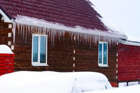 Many large and sharp icicles hang on the roof of the house. Stock Photos