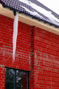 Many large and sharp icicles hang on the roof of the house. Stock Photos