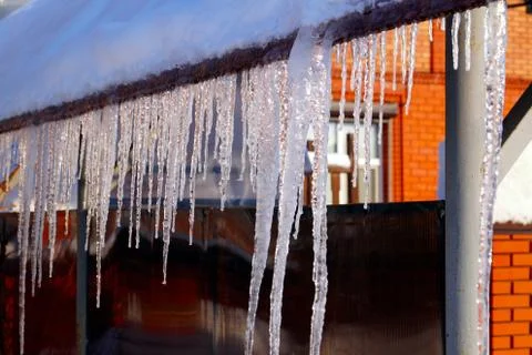 Many large and sharp icicles hang on the roof of the house. Stock Photos