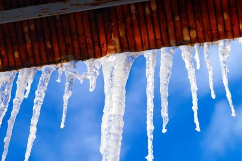 Many large and sharp icicles hang on the roof of the house. Stock Photos