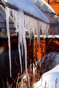 Many large and sharp icicles hang on the roof of the house. Stock Photos