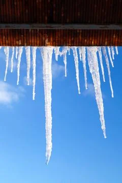 Many large and sharp icicles hang on the roof of the house. Stock Photos