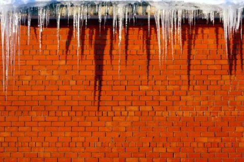 Many large and sharp icicles hang on the roof of the house. Stock Photos