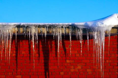 Many large and sharp icicles hang on the roof of the house. Stock Photos