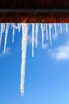 Many large and sharp icicles hang on the roof of the house. Stock Photos