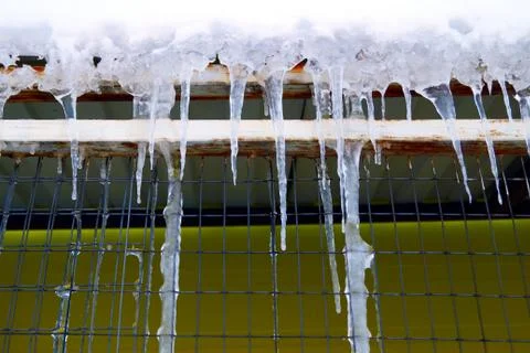Many large and sharp icicles hang on the roof of the house. Stock Photos