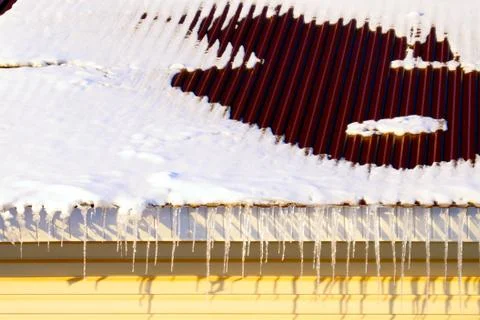 Many large and sharp icicles hang on the roof of the house. Stock Photos