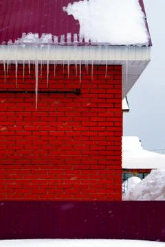 Many large and sharp icicles hang on the roof of the house. Stock Photos