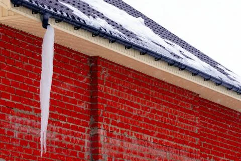 Many large and sharp icicles hang on the roof of the house. Stock Photos