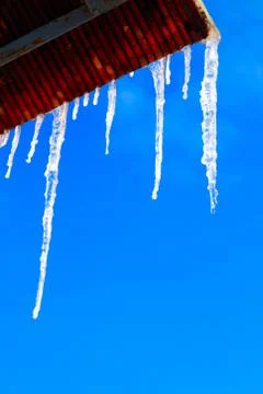 Many large and sharp icicles hang on the roof of the house. Stock Photos