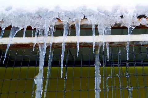 Many large and sharp icicles hang on the roof of the house. Stock Photos