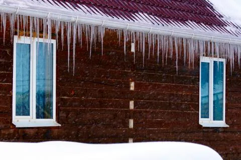 Many large and sharp icicles hang on the roof of the house. Stock Photos