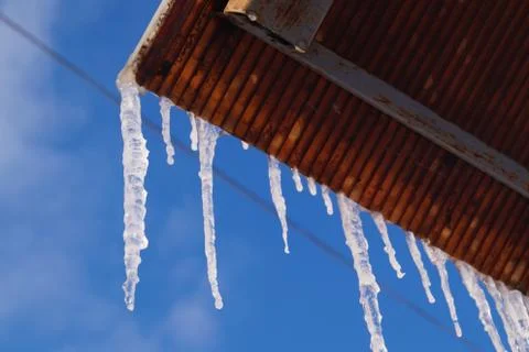Many large and sharp icicles hang on the roof of the house. Stock Photos