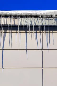 Many large and sharp icicles hang on the roof of the house. Stock Photos